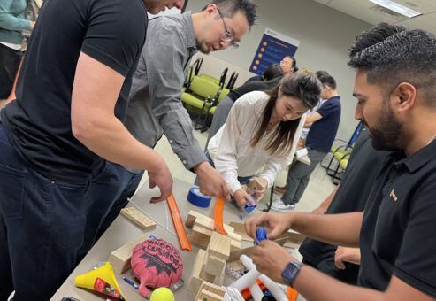 Group of participants collaboratively constructing a Rube Goldberg-style machine during the Domino Effect team building event.