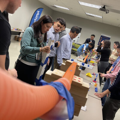 Teams working together to build an intricate Rube Goldberg machine during the Domino Effect team building activity. thumbnail