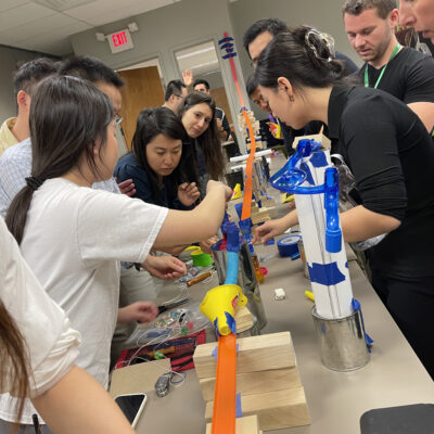 A group of participants collaborates to assemble a complex chain reaction during the Domino Effect team building activity, focusing on constructing innovative contraptions. thumbnail