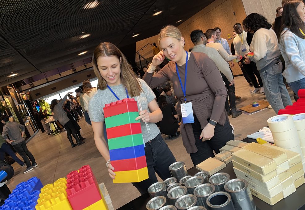 Team members work together during a chain reaction team building activity, assembling large colorful blocks as part of their Rube Goldberg-inspired machine.