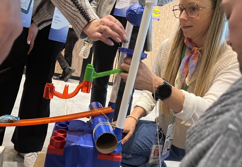 Participants carefully assemble pieces for a Rube Goldberg-inspired machine during a Chain Reaction team building activity, focusing on intricate connections and design.