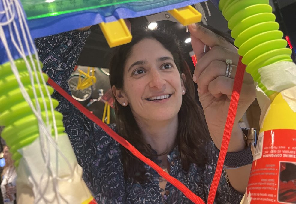 Participant carefully assembles a part of a complex Chain Reaction machine during a team building activity inspired by Rube Goldberg.