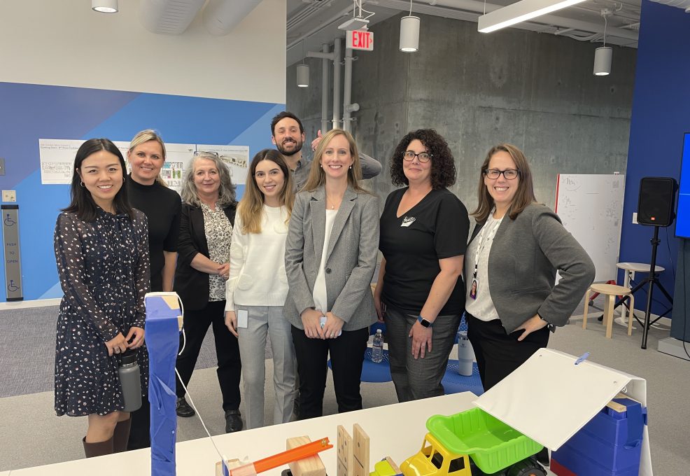 Group photo of team members standing together behind a chain reaction setup during a team building event. The participants are smiling, showcasing a collaborative and friendly atmosphere.