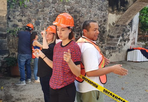 Outdoor team building activity focused on trust and communication. Paired participants wearing safety gear stand back-to-back, using non-verbal cues to complete the challenge, reinforcing teamwork and cooperation.