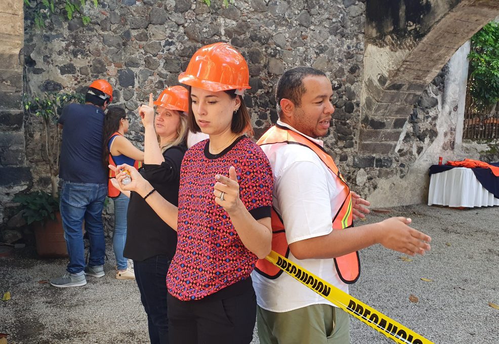 Outdoor team building activity focused on trust and communication. Paired participants wearing safety gear stand back-to-back, using non-verbal cues to complete the challenge, reinforcing teamwork and cooperation.