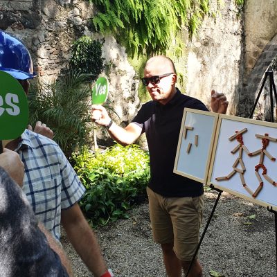 Outdoor team building activity focused on communication and accuracy. Participants use 'yes' signs to provide feedback while teammates construct a model, emphasizing teamwork, strategy, and clear instructions. thumbnail