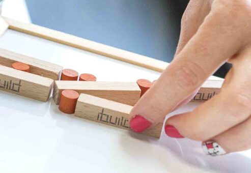 Close-up of a participant assembling an 'ibuild' model during a team building activity. The exercise emphasizes precision, communication, and collaboration to successfully recreate the structure.