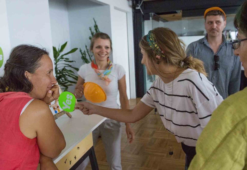 Team building activity focused on communication and collaboration. Participants use 'yes' signs to provide real-time feedback, reinforcing the importance of clear instructions and teamwork in achieving a shared goal.