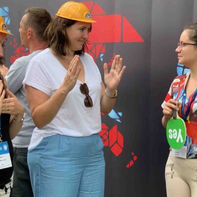 Team building activity focused on non-verbal communication. Participants wearing hard hats use gestures to convey a message while receiving feedback, emphasizing teamwork, clarity, and collaboration. thumbnail