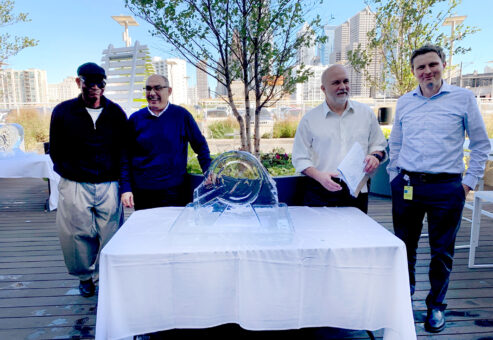 A group of participants proudly poses next to their completed ice sculpture, showcasing their teamwork and creativity during a Team building Ice Sculpting event.