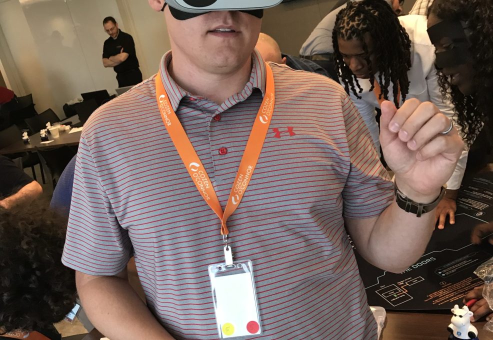 A participant wearing a VR headset labeled '5' engages in The Infinite Loop team building activity, immersing in a virtual reality experience during the event.