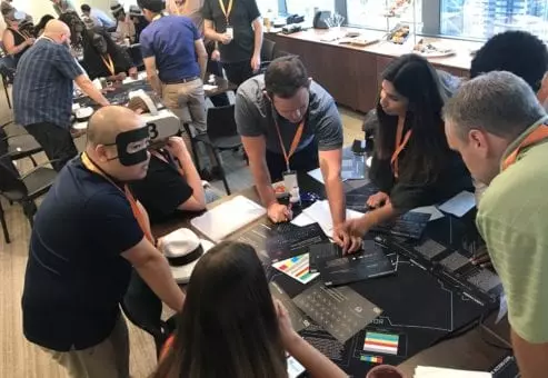 Participants gather around a table during The Infinite Loop team building event, collaborating to solve virtual puzzles as part of a VR-based challenge.