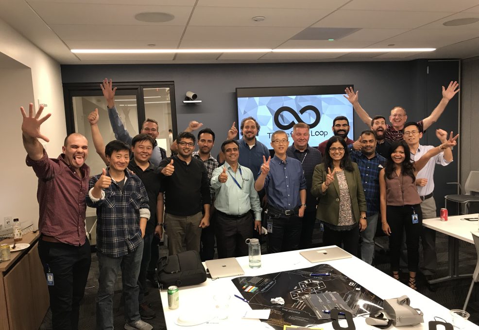 A group of participants enthusiastically pose with raised hands at the conclusion of The Infinite Loop team building event.