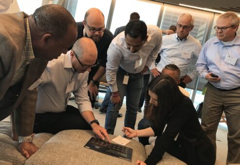 A team gathers closely around a puzzle board during The Infinite Loop team building event, collaborating to solve a challenge.