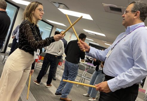 Two participants practicing rhythm coordination with drumsticks during a BeatsWork team building activity.