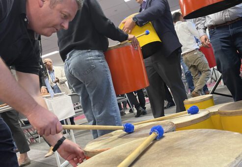 Participants engaged in a drumming session, playing large percussion drums during a BeatsWork team building activity.