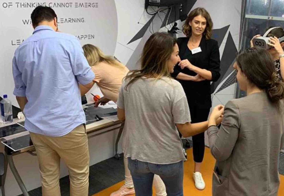 Participants engaging in a collaborative VR challenge at The Infinite Loop team building event, with one member wearing a VR headset while others provide input and work together.