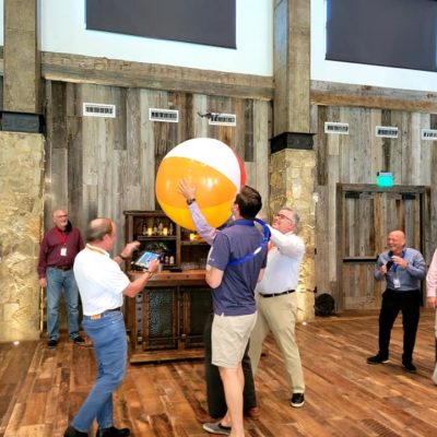 Participants work together to keep a giant beach ball in the air during a lively team building activity, fostering collaboration and fun. thumbnail