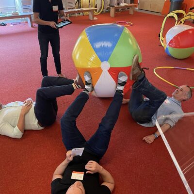 Participants engage in a creative problem-solving challenge during the Game of Drones team building event, using teamwork to maneuver a large beach ball. thumbnail