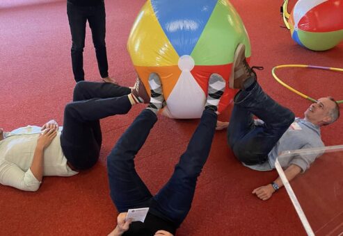 Participants engage in a creative problem-solving challenge during the Game of Drones team building event, using teamwork to maneuver a large beach ball.