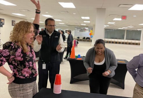 Participants enthusiastically reacting and cheering during a cup stacking challenge in the In It to Win It team building game, displaying excitement, competitive spirit, and teamwork.