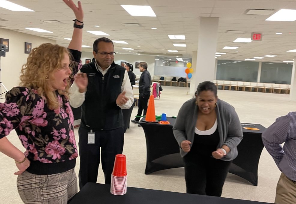 Participants enthusiastically reacting and cheering during a cup stacking challenge in the In It to Win It team building game, displaying excitement, competitive spirit, and teamwork.