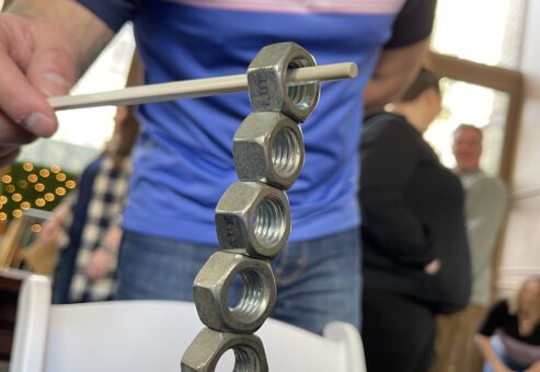 A close-up of a participant carefully balancing metal nuts on a table using a chopstick during the In It to Win It team building challenge, demonstrating precision, focus, and steady hands.