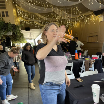 A participant engaged in a pencil flipping challenge during the In It to Win It team building game, focusing intently while attempting to catch multiple pencils in one hand, showcasing coordination and agility. thumbnail