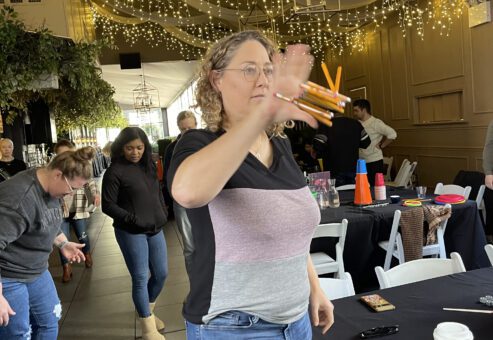 A participant engaged in a pencil flipping challenge during the In It to Win It team building game, focusing intently while attempting to catch multiple pencils in one hand, showcasing coordination and agility.