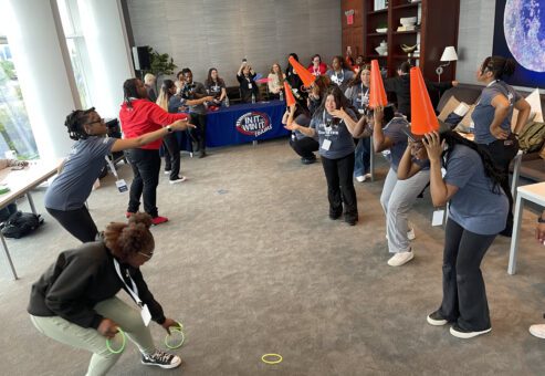 Participants engaged in a lively ring toss challenge, with some wearing traffic cones on their heads as targets, during the In It to Win It team building game, creating a fun and energetic atmosphere.