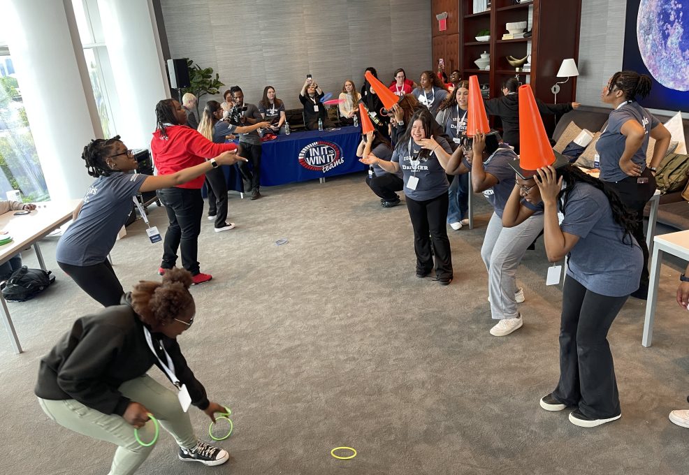 Participants engaged in a lively ring toss challenge, with some wearing traffic cones on their heads as targets, during the In It to Win It team building game, creating a fun and energetic atmosphere.