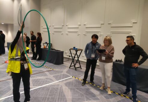 A participant guides a drone through a hula hoop obstacle while teammates monitor and strategize during the Game of Drones team building event.
