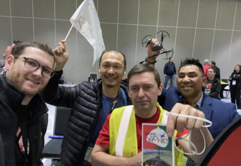 A group of drone pilots proudly display their pilot badge and drone during the Game of Drones team building event, ready for some high-flying fun and competition.