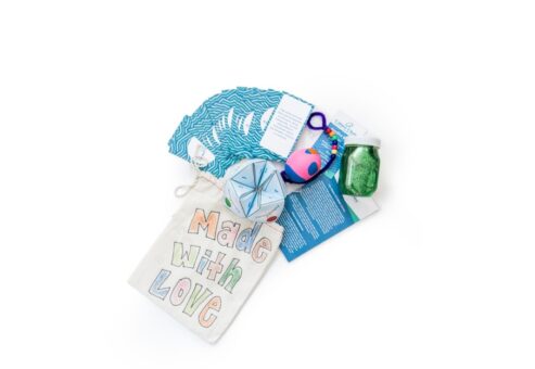 A collection of colorful craft items, including a bag labeled Made with Love, a glitter jar, and various playful objects.