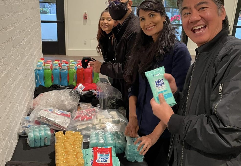 Participants smile while assembling personal care kits during the Helping Hands team building event. They work together to organize hygiene products and snacks for community members in need.