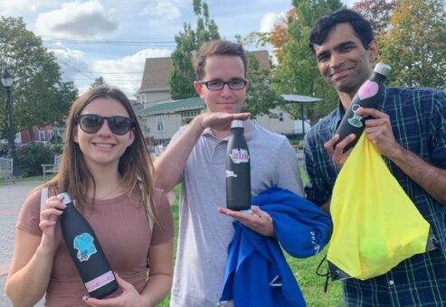 Three participants proudly displaying decorated water bottles and donation bags during the Healthcare Heroes scavenger hunt team building activity.