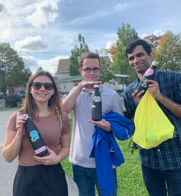 Three participants proudly displaying decorated water bottles and donation bags during the Healthcare Heroes scavenger hunt team building activity.