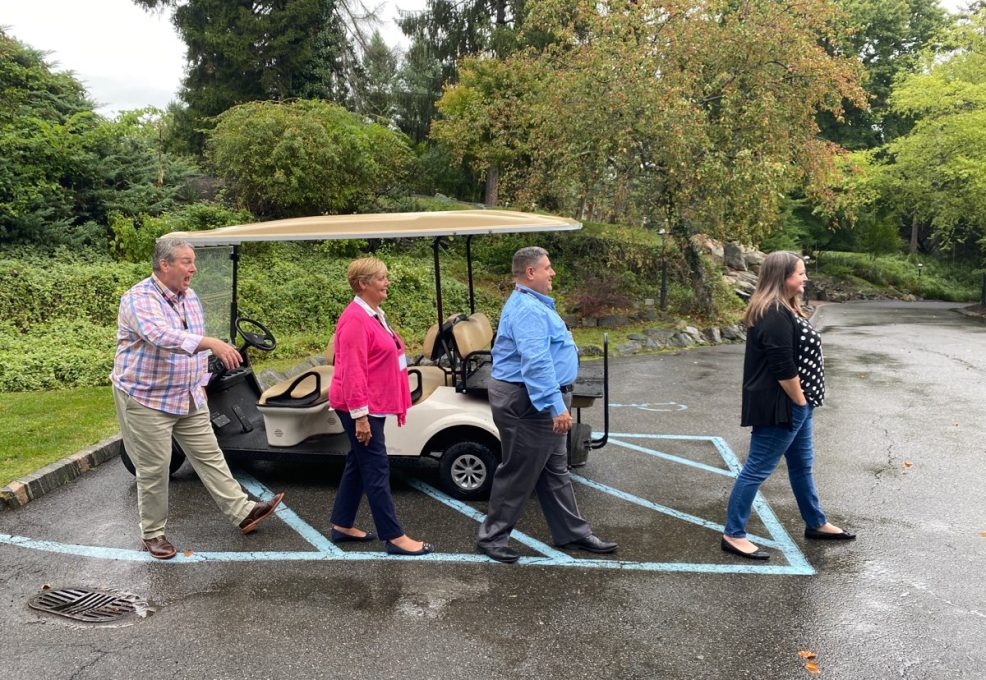 Team members recreate the iconic Abbey Road crossing in a lighthearted moment during the Healthcare Heroes team building event. Four participants walk in a line in front of a golf cart, mimicking the famous Beatles pose, bringing fun and engagement to the event which embraces Corporate Social Responsibility by supporting local healthcare professionals.
