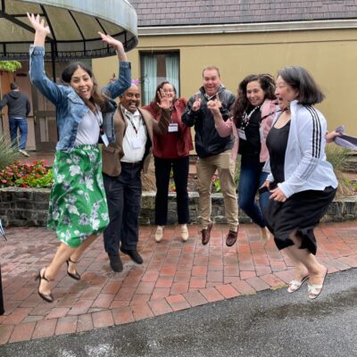 Group of seven team members joyfully jumping in the air during the Healthcare Heroes team building event. Participants, smiling and mid-air, embody the fun and energy of the event aimed at supporting healthcare professionals. thumbnail