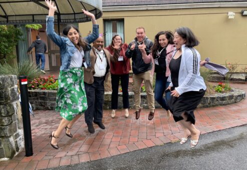 Group of seven team members joyfully jumping in the air during the Healthcare Heroes team building event. Participants, smiling and mid-air, embody the fun and energy of the event aimed at supporting healthcare professionals.