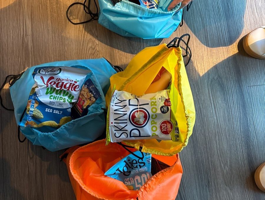 Colorful drawstring bags filled with healthy snacks such as veggie chips, pistachios, and popcorn, ready to be donated as part of the Healthcare Heroes scavenger hunt team building program.