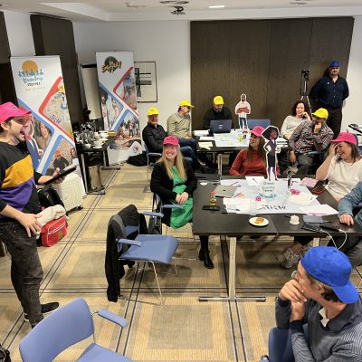 Team members actively participating in the Leadership Stories game, wearing colorful hats and engaging in discussions, creating a fun and interactive learning environment. thumbnail