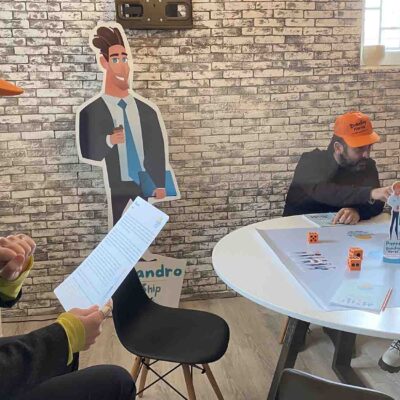 Participants engaged in a Leadership Stories team building activity, with one team member reading instructions while others play the game. thumbnail