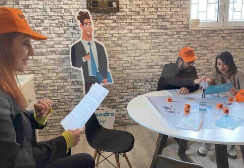 Participants engaged in a Leadership Stories team building activity, with one team member reading instructions while others play the game.