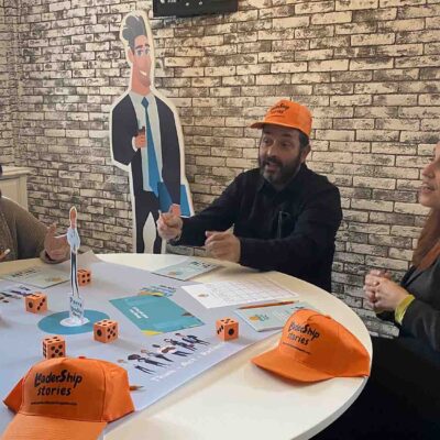 Participants engage in a Leadership Stories game, discussing and making leadership decisions, while wearing branded hats and working together at a table. thumbnail