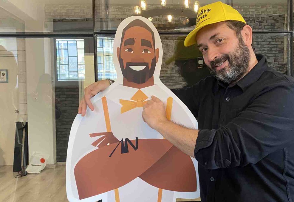 A team member posing with their Leadership Stories game character, smiling and pointing at the cutout.