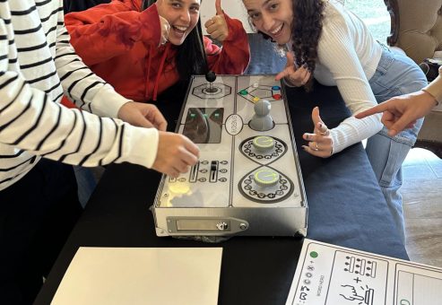 Excited participants smile and give thumbs up while engaging in a retro Team Synergy gaming challenge, focusing on teamwork and strategy.