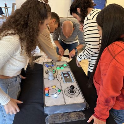 Team members gather around the Team Synergy gaming console, collaborating and strategizing during a hands-on team building activity. thumbnail