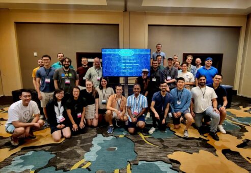 A large group of participants pose together in front of a Team Synergy retro gaming screen after a successful team building event, celebrating collaboration and teamwork.