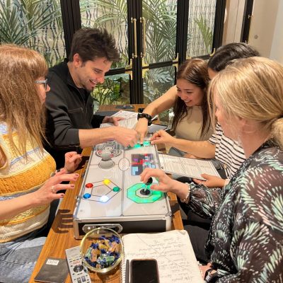 A group of participants working together on a Team Synergy retro gaming console, solving puzzles and collaborating during a team building activity. thumbnail